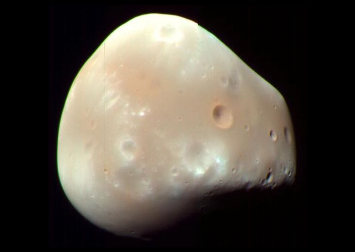 Deimos is not as cratered as Phobos but still contains some craters on the surface, the shallower looking craters appear lighter in color, taking on a white/gray hue compared to the darker orange larger/deeper craters.
