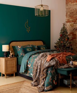 A bedroom with green wall paint decor, Christmas tree, rattan and black framed headboard and rattan side table with jute rug