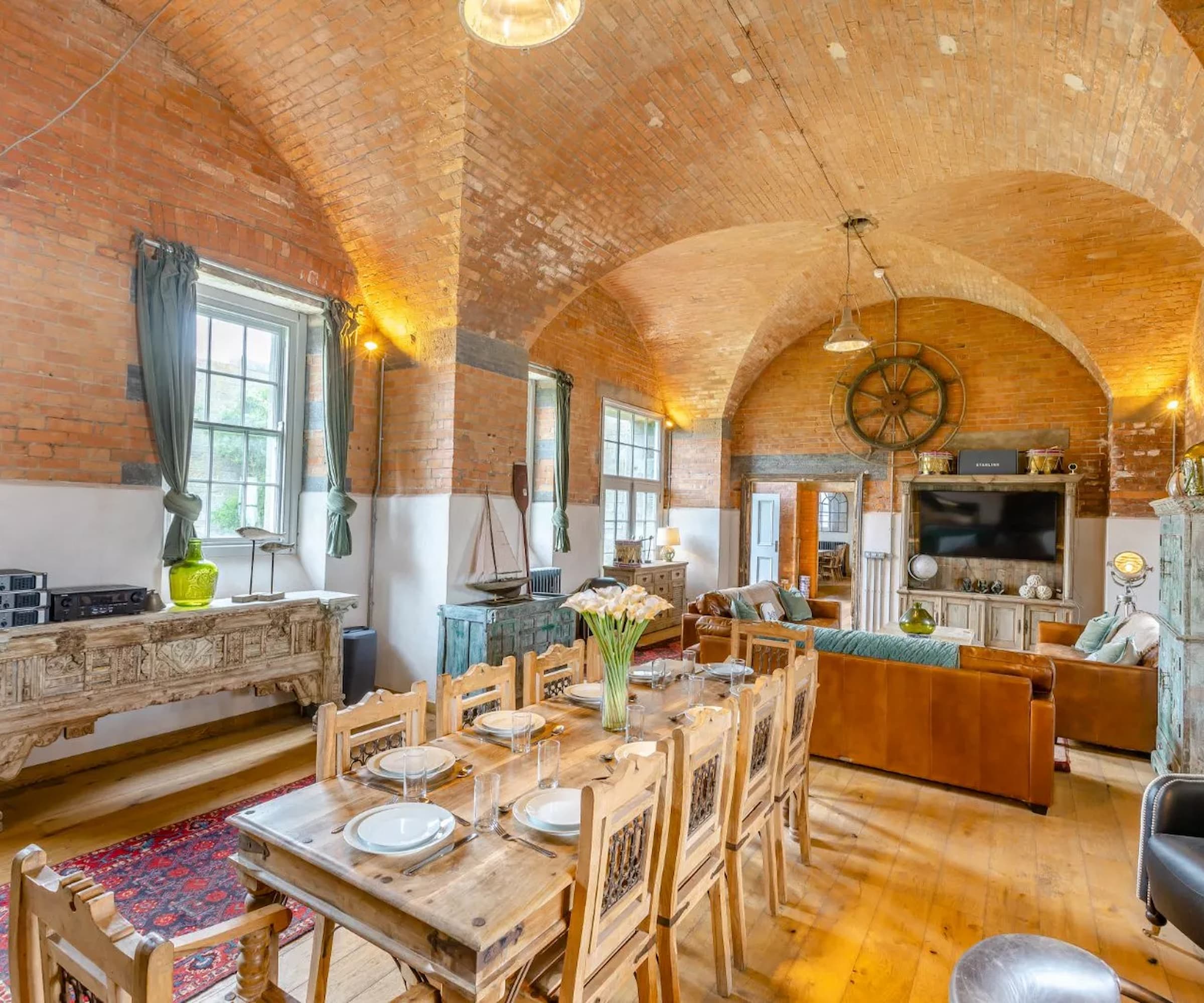 A kitchen-diner with a curved ceiling with a large wooden dining table and brick walls