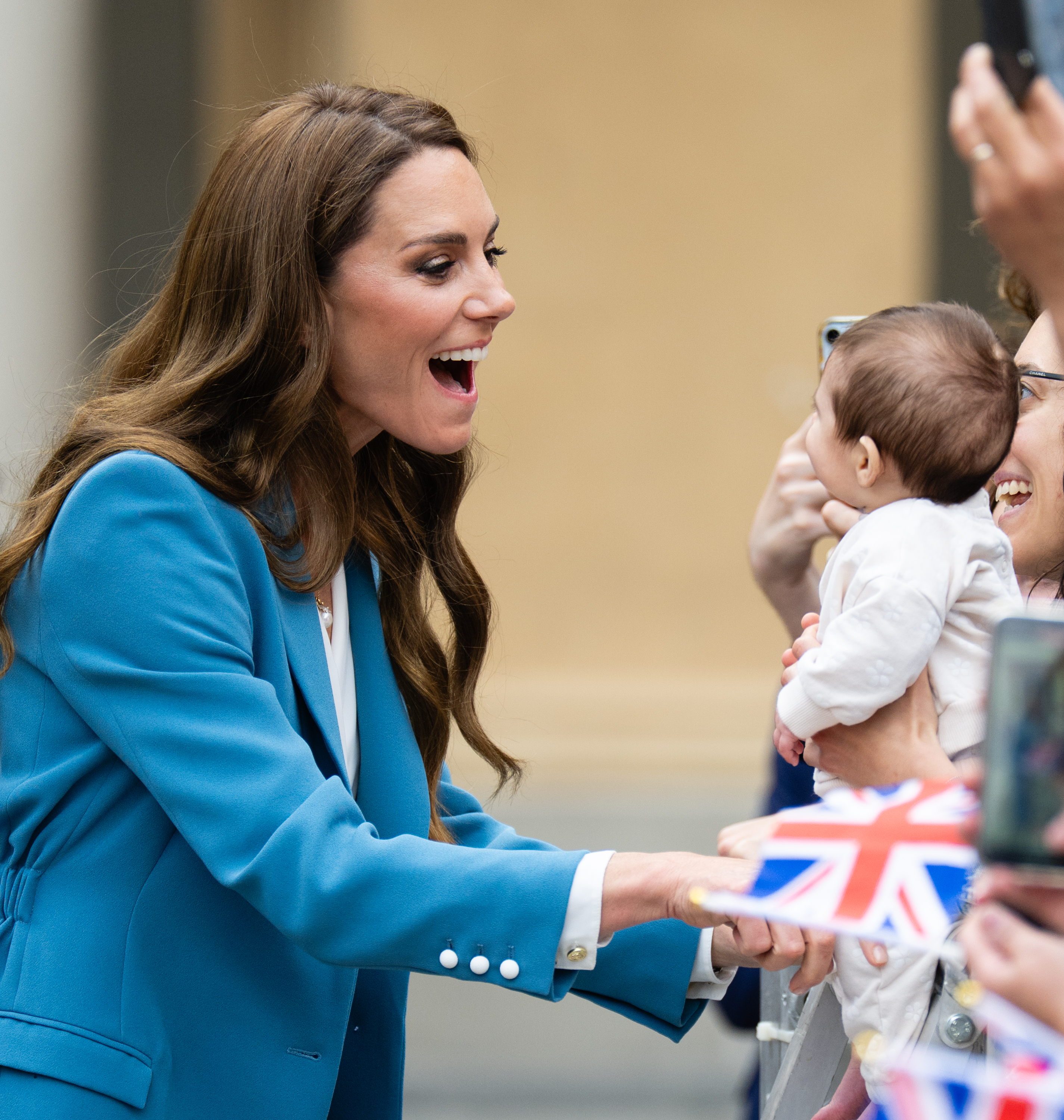 Princess Kate wearing a blue suit smiling at a baby