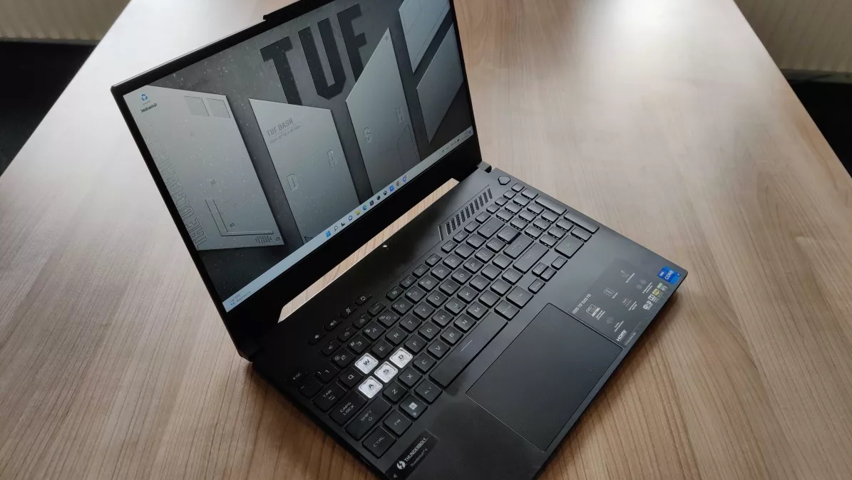 Asus TUF Dash F15 laptop on wooden table with screen open showing Windows 11 desktop