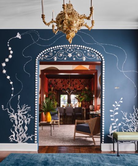 Blue entryway with blue painted walls and white flower murals, looking through and arch doorway into a orange living room with furniture and large neutral rug