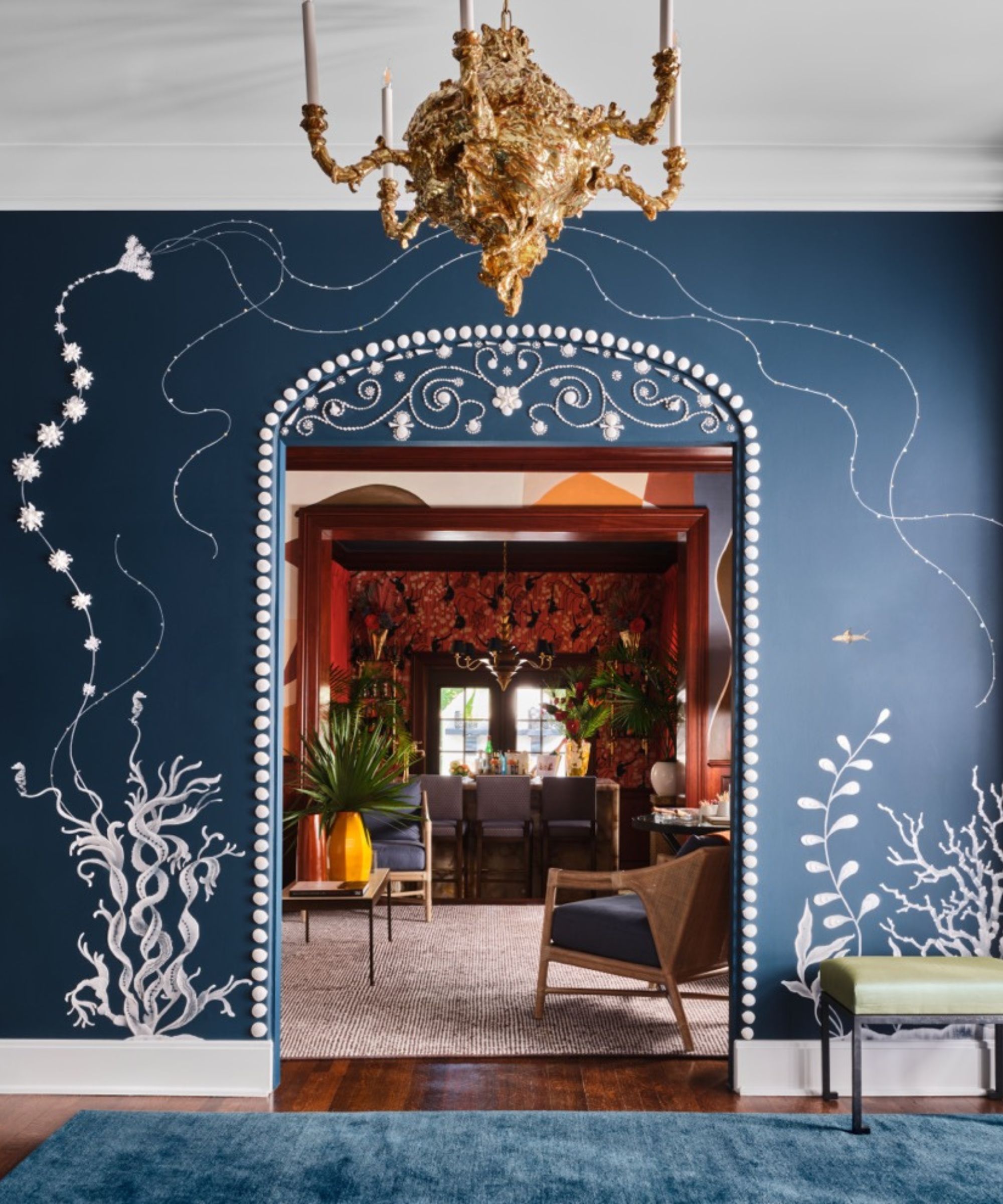 Blue entryway with blue painted walls and white flower murals, looking through and arch doorway into a orange living room with furniture and large neutral rug