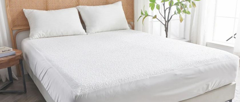 The image shows the SiJo AiryWeight Eucalyptus Mattress Protector placed on a mattress against a rattan bed frame 