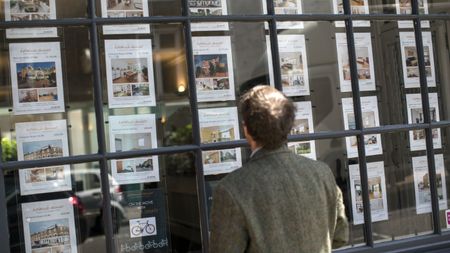 A potential home buyer looks at properties displayed in an estate agent window 