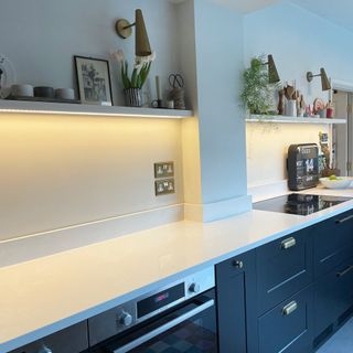 LED lighting strip underneath an open shelf in a grey and white kitchen