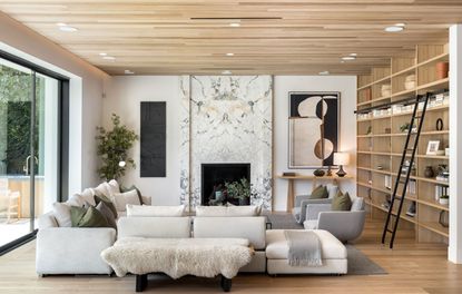 living room with pale wood floor and ceiling with bookcase and ladder and white sectional sofa and marble clad fireplace