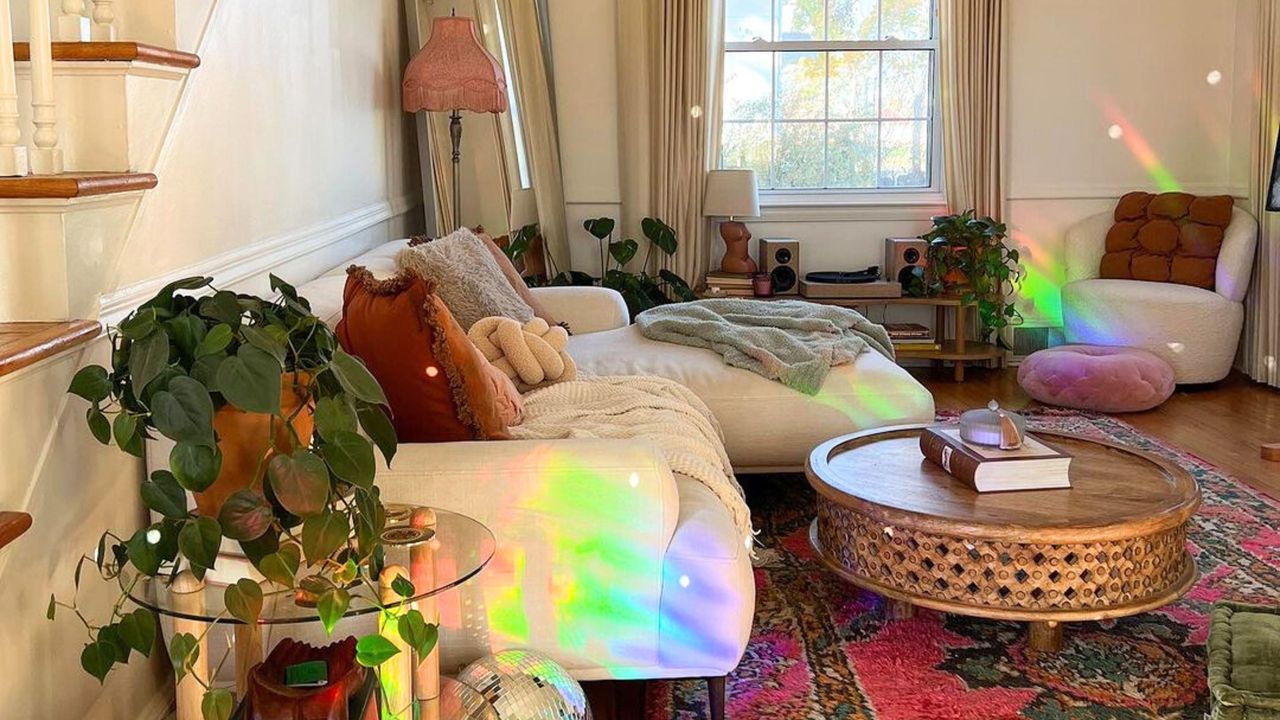 A small living room with a rainbow light, white couch, red geometric rug, coffee table, and a disco ball