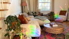 A small living room with a rainbow light, white couch, rug, coffee table, and a disco ball