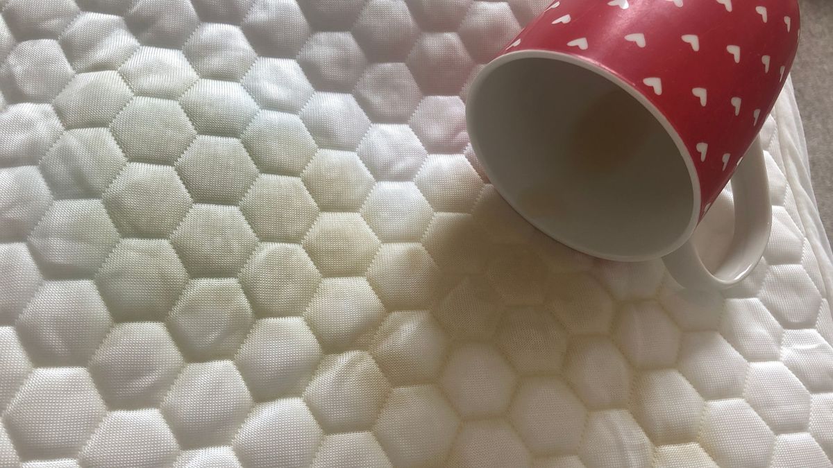 A tipped-over mug spills tea onto a waterproof mattress protector