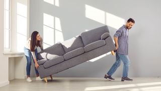 Two people carrying a couch across a room