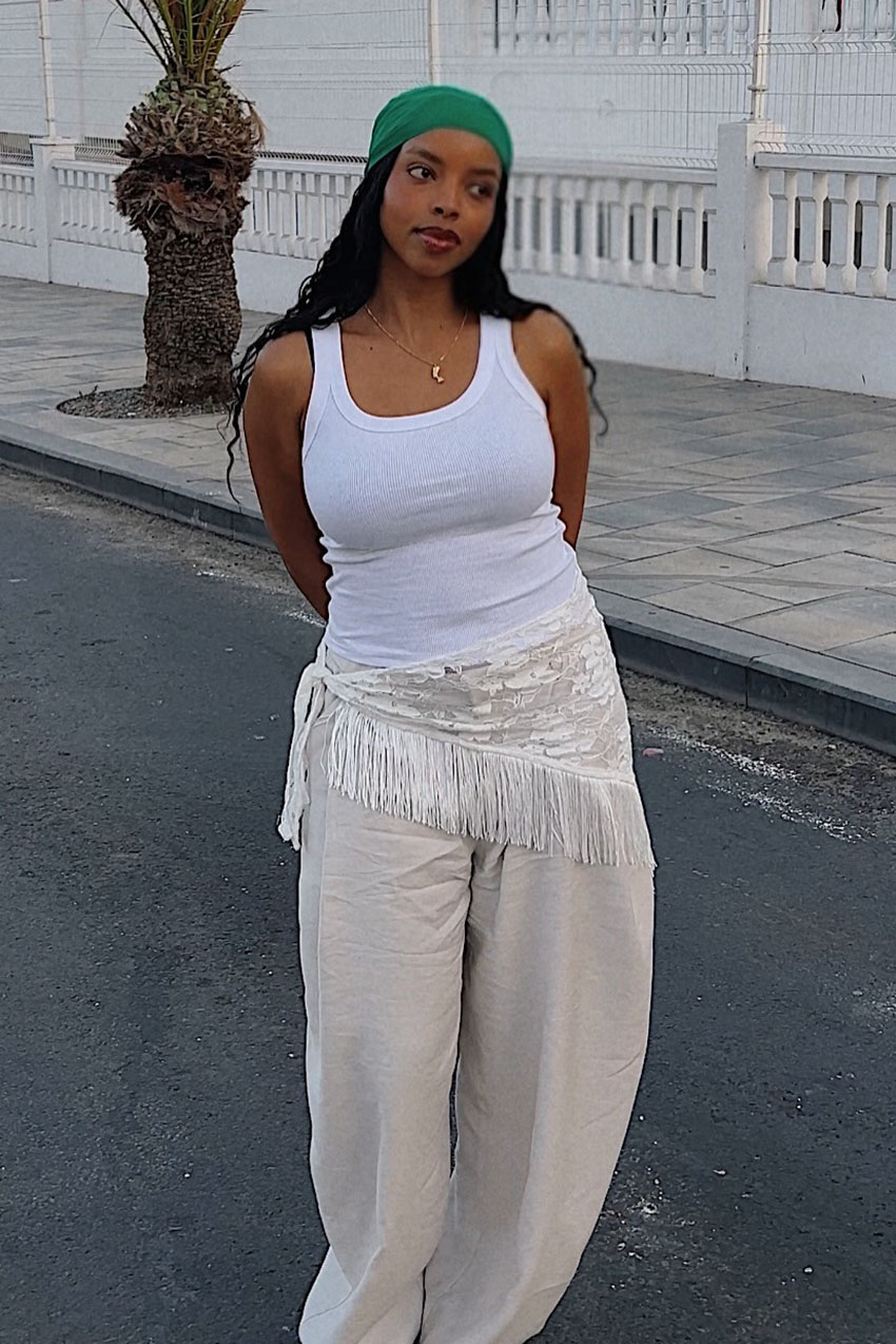 a woman wearing a white tank top and white pants with a fringe scarf and green scarf on her head