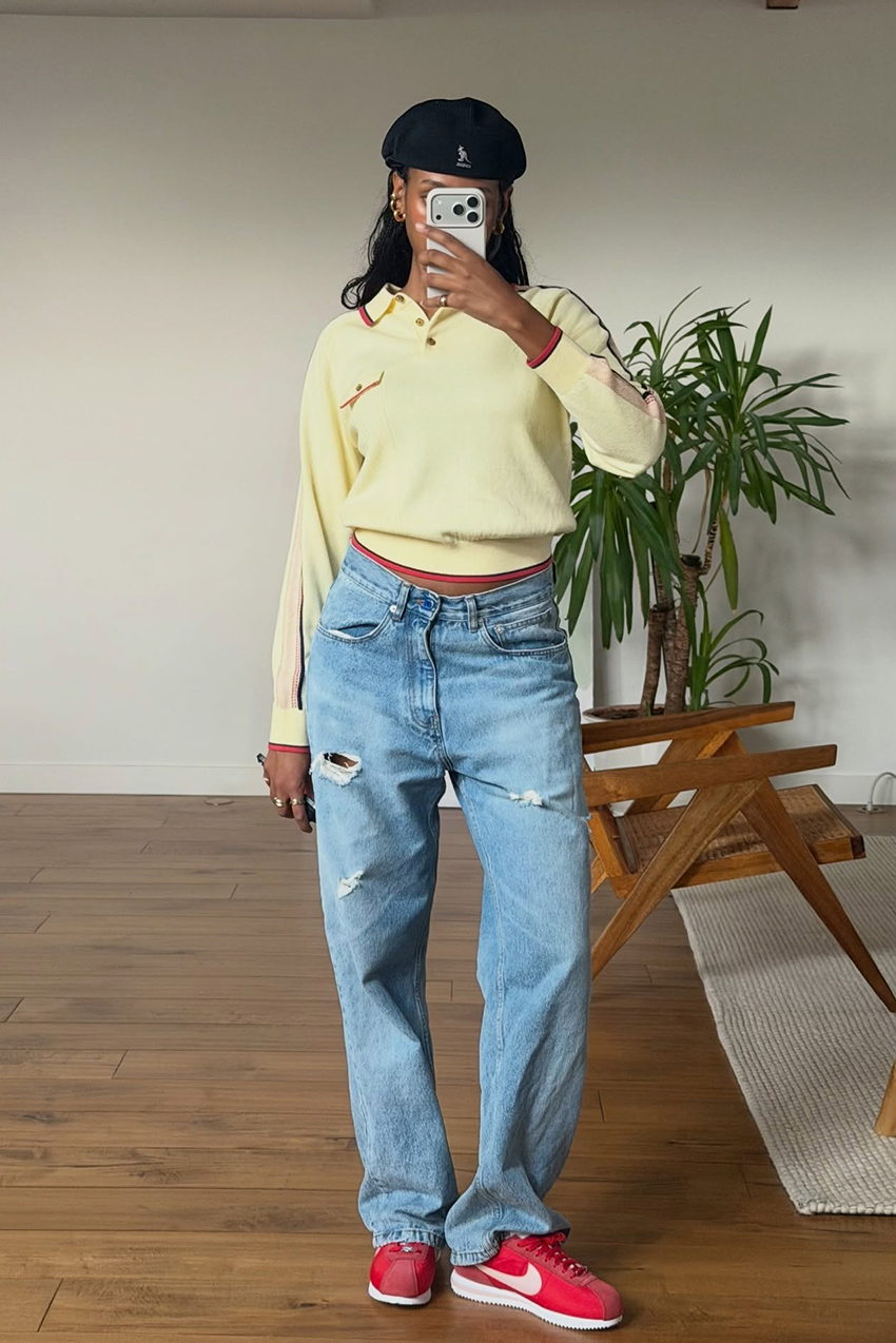 a woman wearing a yellow polo longsleeve, blue jeans, and red sneakers
