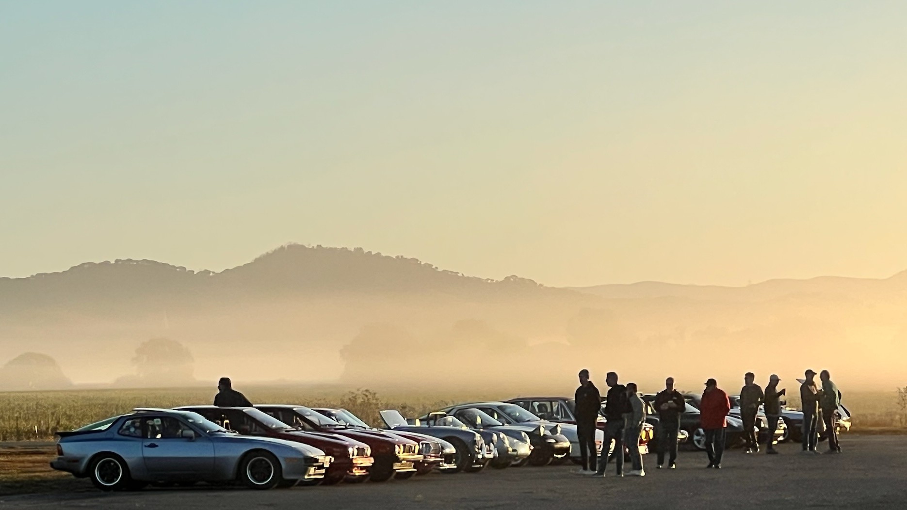 20th century sports classic cars are lined up at an auto event with California mountains and fog in the background.