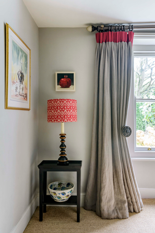 Corner of gray room with gray painted walls, curtains with bright pink trim, matching pink lampshade on black side table