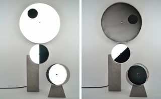 Circular lights. One piece is set on the wall, while the other two are set on gray stands on the floor.