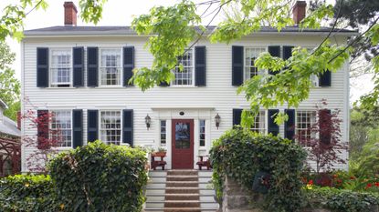 exterior of traditional white wooden colonial house with black shutters and red door