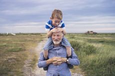 A young boy, hot and sweaty from running around, smiling while being carried by his grandad on an evening walk through a coastal salt marsh.