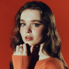 Carrie actress Summer Howell photographed by Jonny Marlow. She is looking to camera, her hand under her chin with a bow diamond ring on her middle finger. She is wearing an orange sweater.