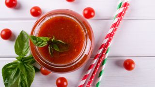 Tomato juice with basil garnish in a glass with straws lying next to it