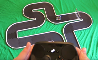 A person holding a Steam controller while driving a small car around a track