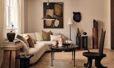 Beige living room with white curved corner sofa, black coffee table and armchair, brown abstract art and black pendant light