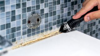 Old caulk being removed in bathroom with caulk removal tool