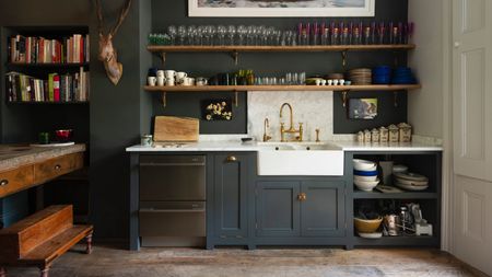 dark blue kitchen open plan, open shelving with glassware, marble backsplash and countertop, white butler sink, wooden floorboards, deVOL