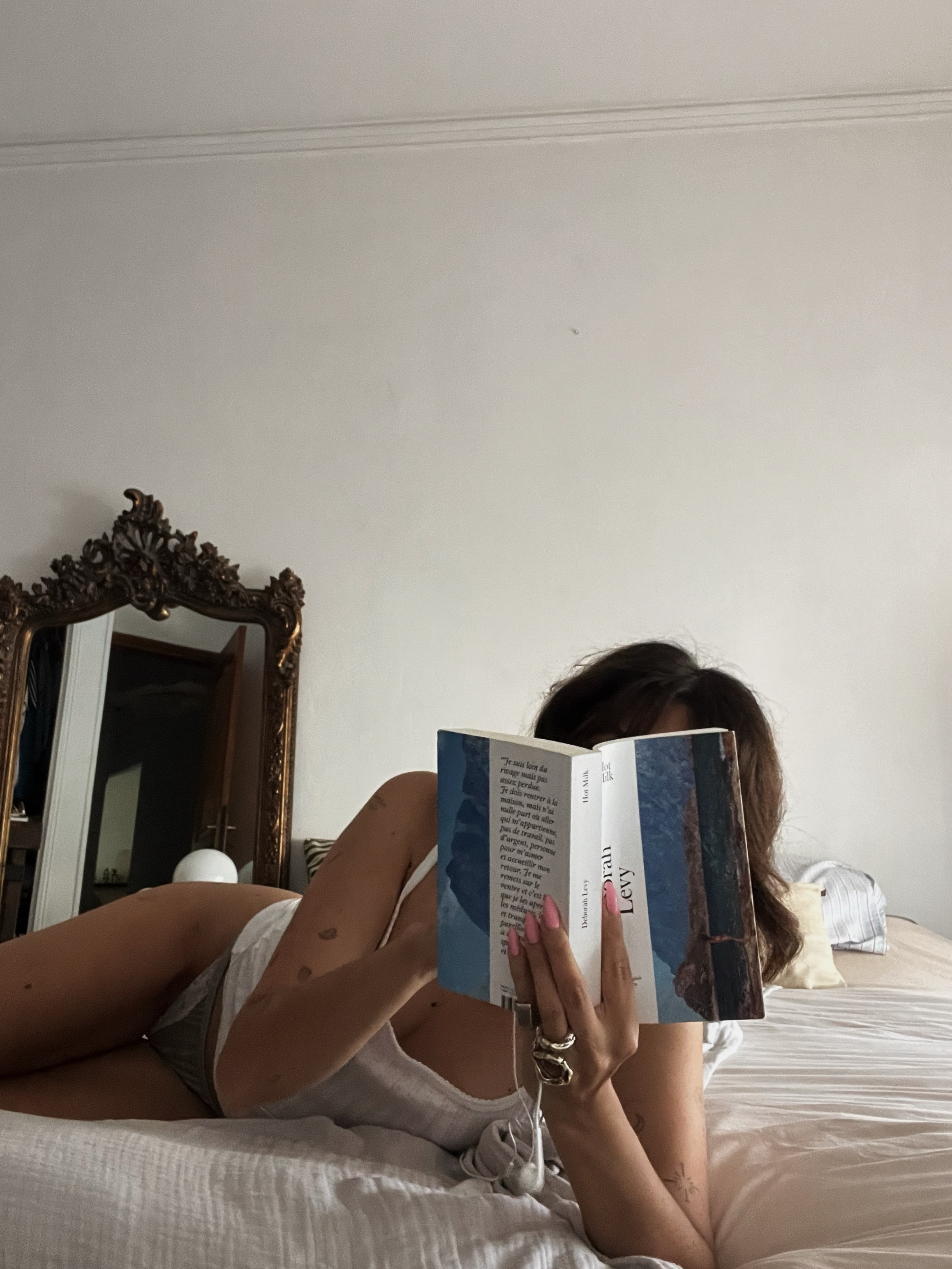 A picture of a bronzed woman reading a book on a bed.