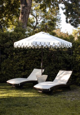 Two white fabric deck chairs on green lawn with scalloped sun umbrella overhead, with black trim