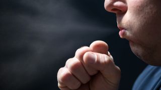 close up photo of a man coughing with a fist barely covering his mouth