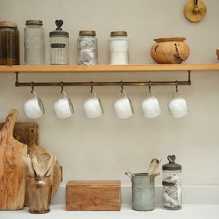 a close up of a kitchen counter with a rustic selection of wooden chopping boards and storage, with a shelf and mug rail