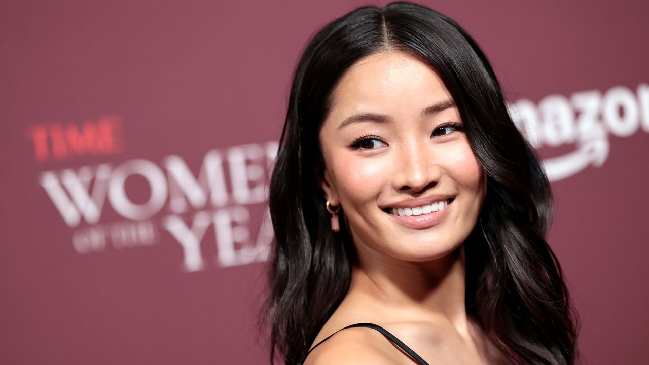 Anna Sawai on a red carpet wearing her hair down with a coach bag