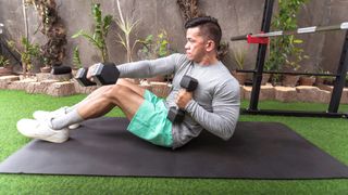 Man on exercise mat performing sit-up punches with right arm forward holding a pair of dumbbells
