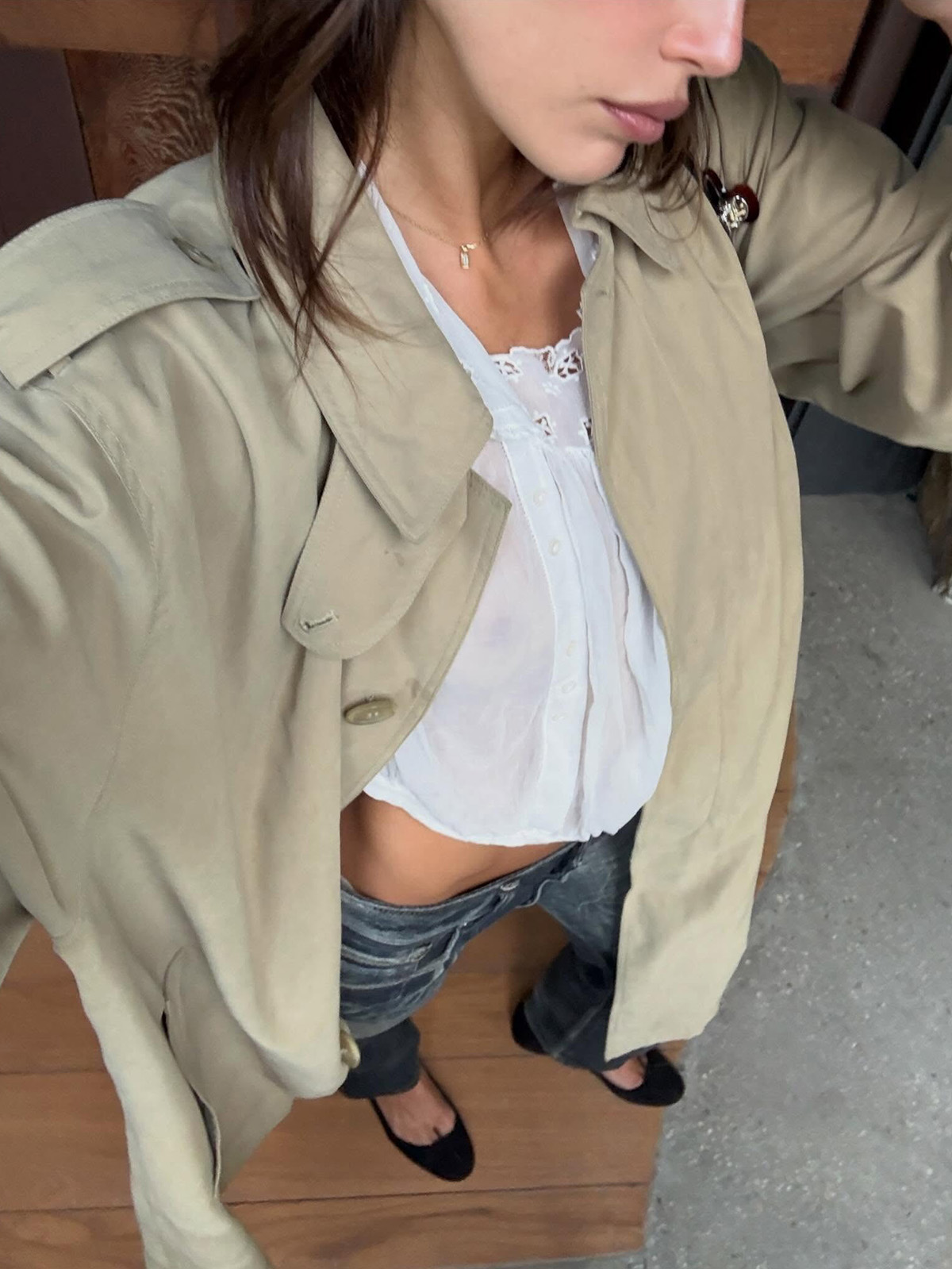 Kaia Gerber wearing a trench coat, white blouse, black jeans, and ballet flats.