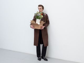 Man in leather trench holding cardboard box of flowers