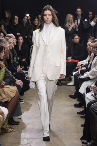 Proenza Schouler model wearing a white suit with a sheer turtleneck layered on top of a white button-down shirt.
