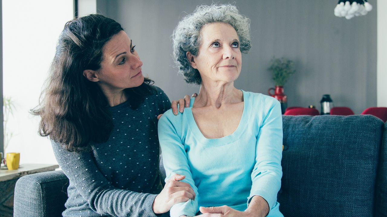 An older woman looks off into the distance, appearing annoyed, while her daughter tries to talk to her.