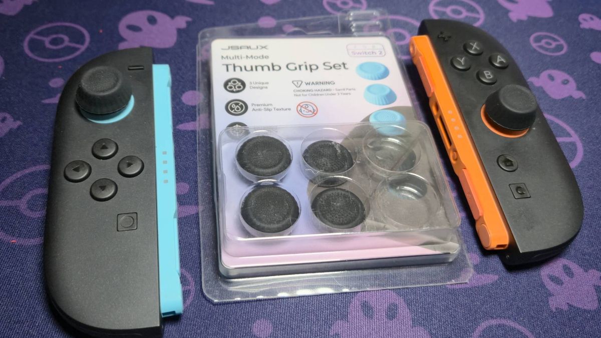 Photo of a pair of Switch 2 Joy-Con sitting on a purple mouse mat, with two high-rise black grips on the sticks.
