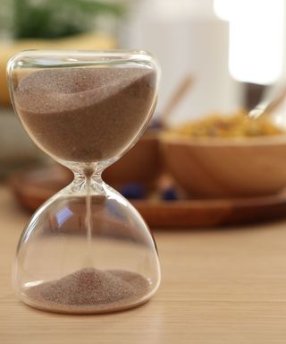 A sand filled hourglass on a kitchen counter, breakfast bowls out of focus in the background