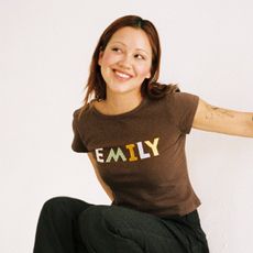 Model wearing Oddli custom baby tee in brown color that says "Emily" in different-colored textiles.