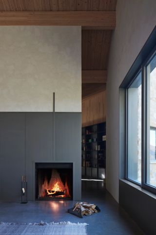 Living room with half limewash, half arey cladded wall with fireplace, concrete floor and wooden rafters