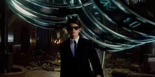 Artemis Fowl wears a suit and sunglasses as he walks away from rubble in a scene from the film.