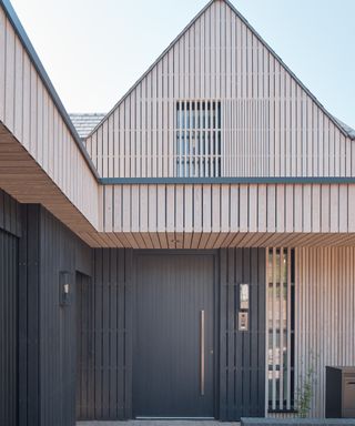 large black slatted front door with long metal handle on modern black and light timber clad contemporary house