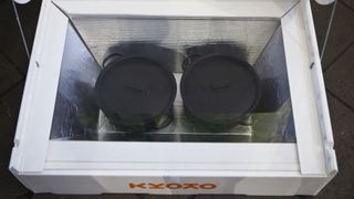 A solar oven reveals two black pots in a box with a plastic lid