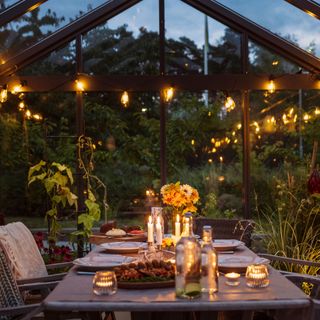A greenhouse lit with candles and set up for a dinner party