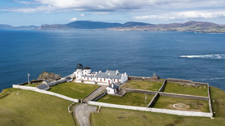 A white light house with attached homes and a stone wall on the coast on looking the ocean