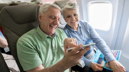 A senior couple on a plane look at a phone together.