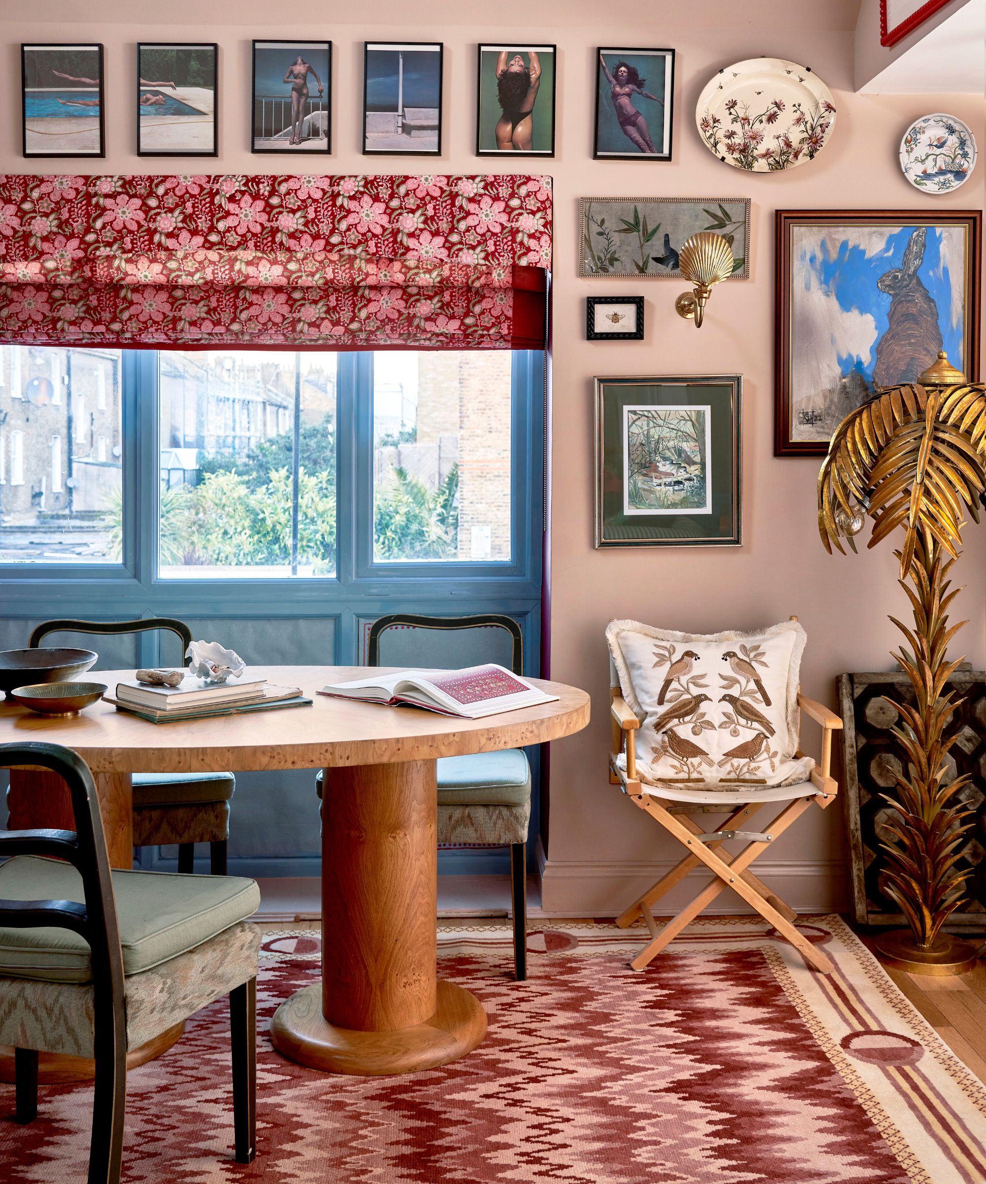 pale pink dining room with blue patio doors, pink floral blind, large burl wood table, mismatched dining chairs and a pink woven rug