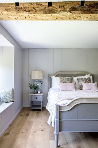 bedroom with gray bed and pink cushions with old ceiling beam and pale wood floors